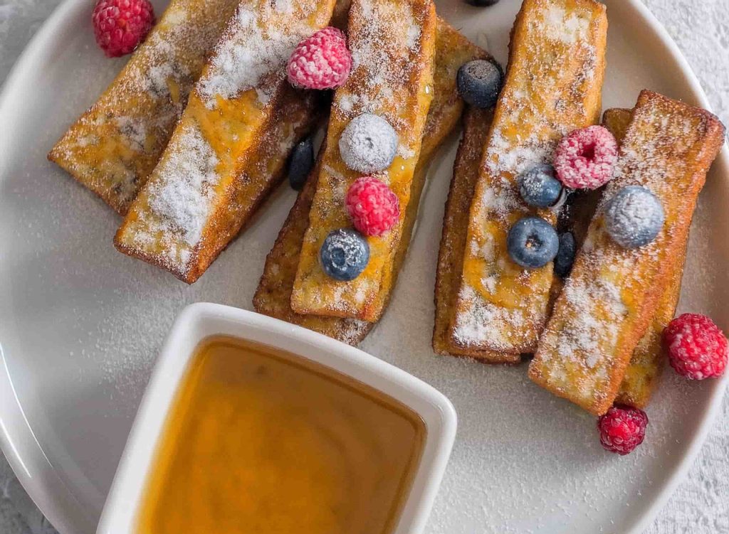 Crispy and Irresistible Frozen French Toast Sticks in Air Fryer 16 A plate of crispy frozen French toast sticks cooked in an air fryer served with maple syrup and fresh berries.