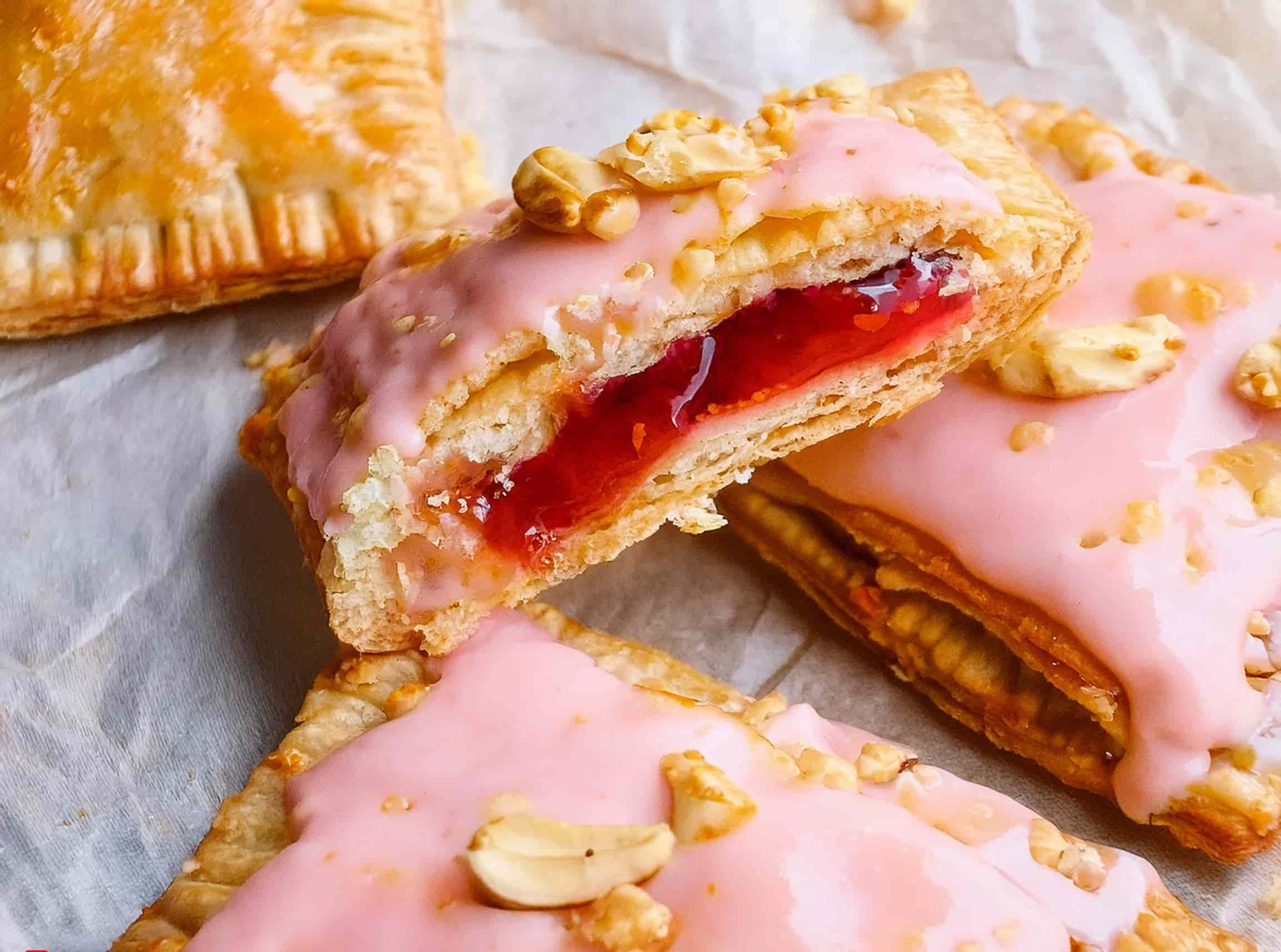Easy Homemade Peanut Butter and Jelly Pop Tarts 17 Homemade peanut butter and jelly Pop-Tarts with golden crusts and a glossy glaze, garnished with chopped peanuts and served on a rustic plate.