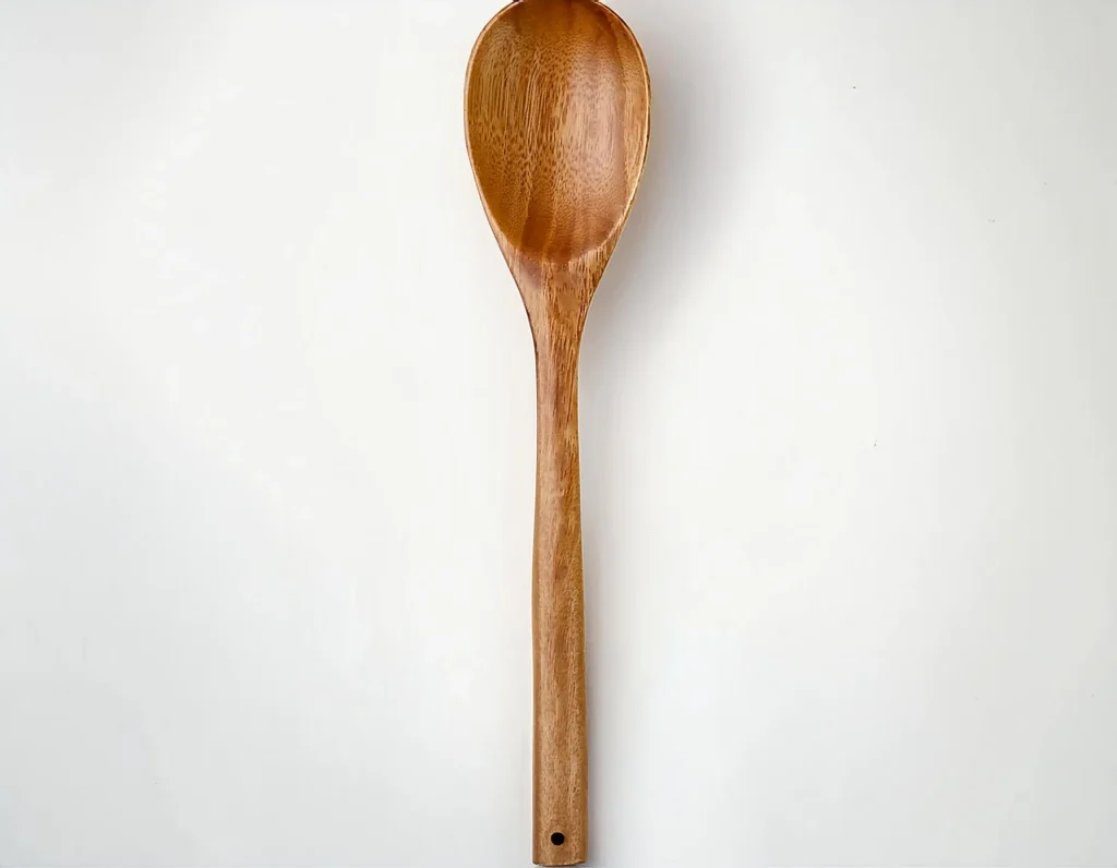 Le Creuset Revolution Solid Best Wooden Spoons resting on a rustic wooden countertop, showcasing its elegant design and beechwood finish.